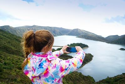 © JosManuel / Adobe Stock - Fille prenant en photo le Lagoa do Fogo - Sao Miguel - Acores - Portugal Fille prenant en photo le Lagoa do Fogo - Sao Miguel - Acores - Portugal