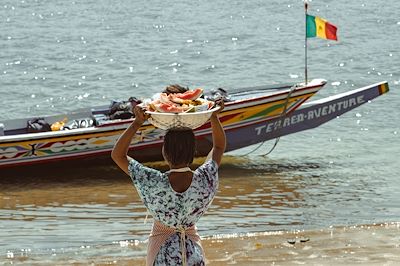 Personne portant une panière de fruits face à la mer au Sénégal